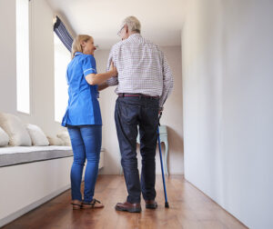 Nurse helping senior man walk using a walking stick