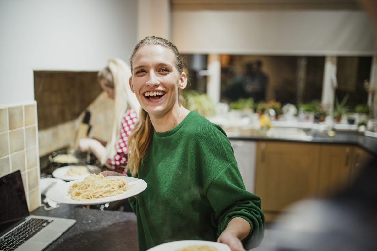 A woman is posing for a photo and smiling in her home kitchen. She is holding plates of food.